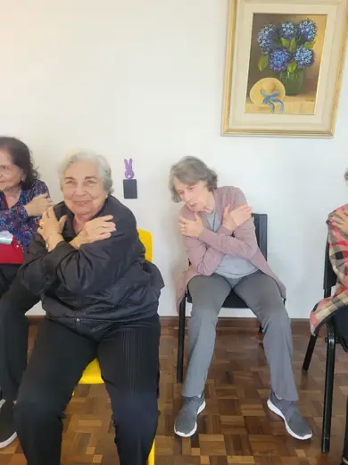 Duas senhoras sentadas em roda, alongando o braço cruzado sobre o peito