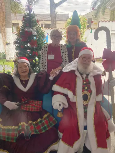 Senhoras vestidas de Mamãe e Papai Noel posando ao lado da árvore de Natal