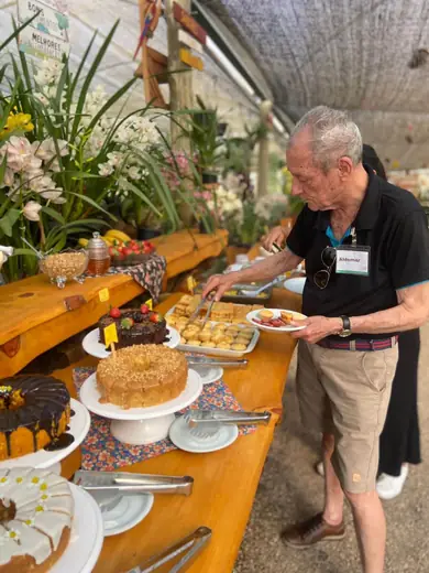 Senhor se servindo na mesa de bolos e doces da festa, na área externa coberta